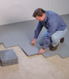 Contractors installing basement subfloor tiles and matting on a concrete basement floor in Tuscaloosa, Alabama